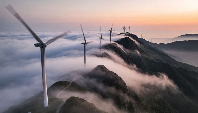 Spinning wind turbines lining foggy mountain ridge with winding road at sunrise