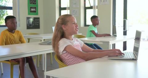 Diverse classmates using laptops in bright modern classroom for digital learning and collaboration