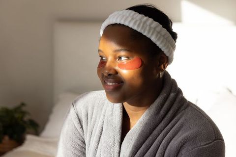 African american woman enjoying skincare with red hydrogel under-eye patches, bathrobe