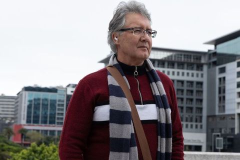 Mature man wearing striped scarf and wireless earbud on city waterfront under cloudy sky