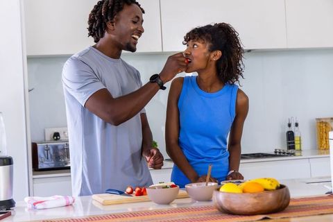 Couple preparing healthy breakfast feeding strawberry morning routine in bright kitchen
