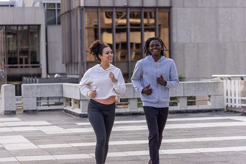 Diverse friends jogging on urban rooftop plaza wearing hoodies and smartwatch, smiling