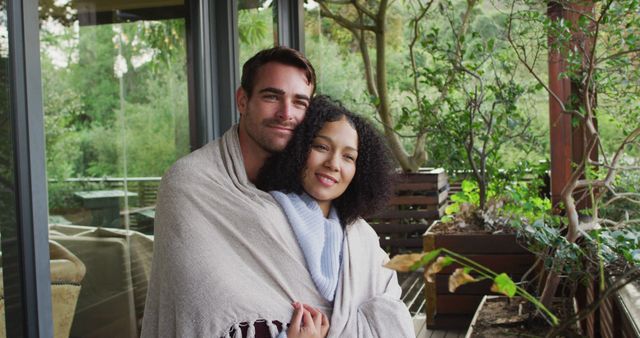 Smiling biracial couple wrapped in sheets embracing each other in the balcony at vacation home. couple honeymoon and vacation concept