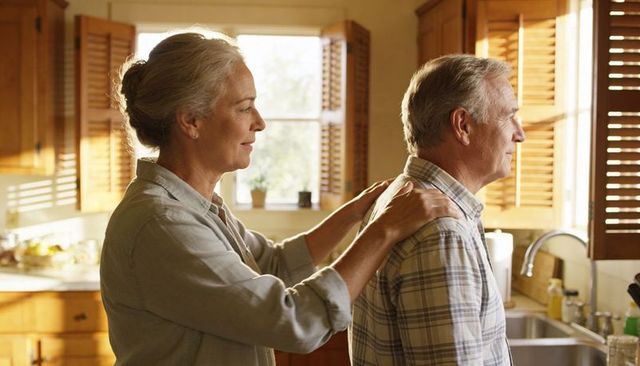 Senior couple sharing tender moment in sunlit kitchen, woman touching partner's shoulders