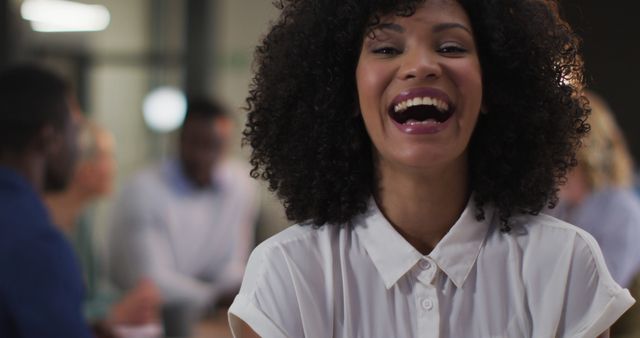 Woman with curly hair laughing in an office environment. Perfect for illustrating positive workplace culture, team spirit, human resources materials, or advertisements. Can be used for websites, blogs, articles about business, office life, motivation, and happiness at work.