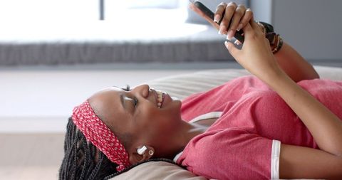 Cheerful Young Woman Smiling While Using Smartphone with Earbuds