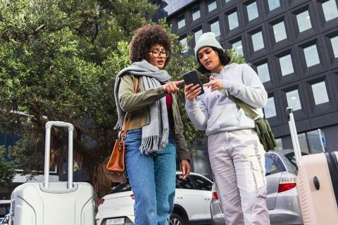 Two Friends Checking Phone for Directions with Rolling Luggage on Urban Curbside