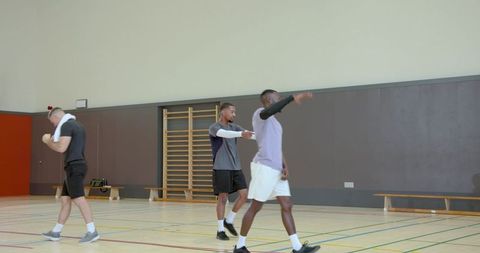 Men walking and gesturing during indoor basketball team practice on wooden gym court