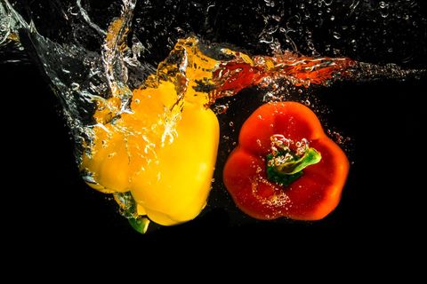 Yellow and red bell peppers splashing in water on black background