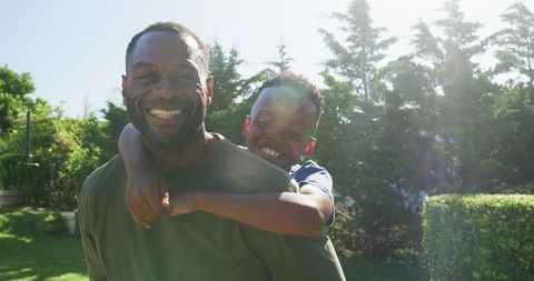 African american father giving son piggyback in sunny backyard laughing and bonding