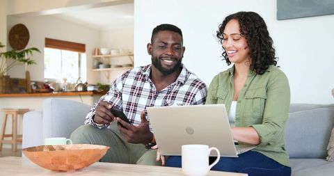 Diverse Couple Collaborating with Smartphone and Laptop in Modern Home