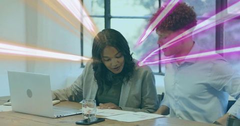 Colleagues reviewing documents with laptop and neon light streaks in sunlit office