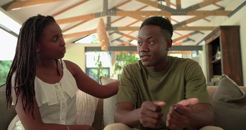 African couple having heartfelt conversation on sunlit modern living room sofa