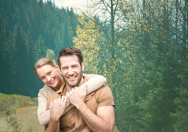A cheerful couple is hugging and smiling in a forested mountain area. The backdrop features lush trees and possible autumn colors, indicating a connection with nature. This image can be used to convey love, happiness, and outdoor enjoyment, ideal for nature blogs, romance or relationship articles, travel advertisements, and lifestyle promotions.