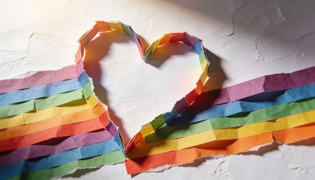 Forming heart from torn rainbow paper strips on textured off-white surface