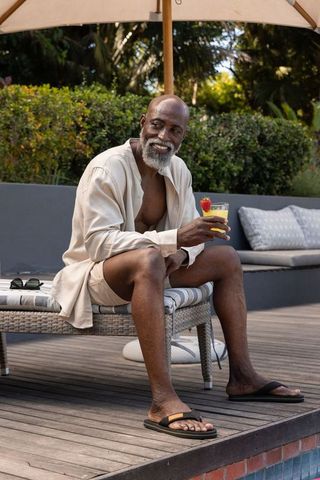 Mature african man relaxing poolside with tropical cocktail wearing linen shirt and shorts