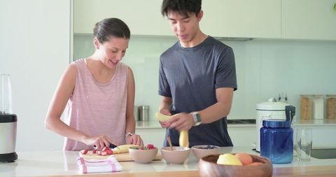 Young multicultural couple preparing fresh fruit bowls in bright modern minimalist kitchen