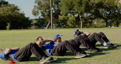 Baseball players doing core training sit-ups on grass field with coach using whistle