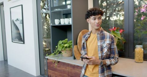 Young Man with Earbuds Checking Smartphone in Modern Kitchen