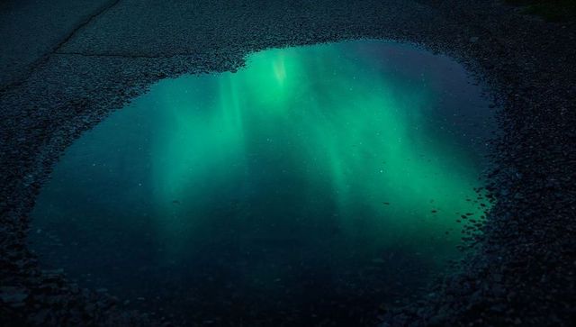 Puddle Reflecting Northern Lights over Cracked Asphalt at Night with Teal Aurora Glow