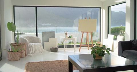 Sunlit coastal art studio with blank easel, ocean view, minimalist decor and plants