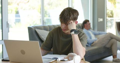 Teen studying at home with laptop and notebook wearing smartwatch and headphones