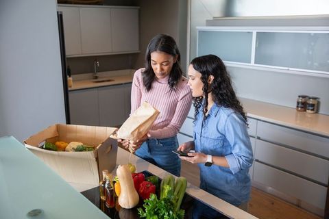 Friends Unpacking Box of Fresh Vegetables and Using Smartphone