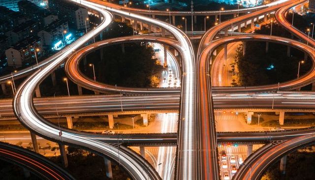 Nighttime aerial view curving multi-level highway interchange with vibrant light trails