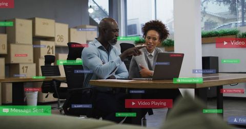 Pointing manager guiding coworker at laptop in modern open-plan office with ar overlays