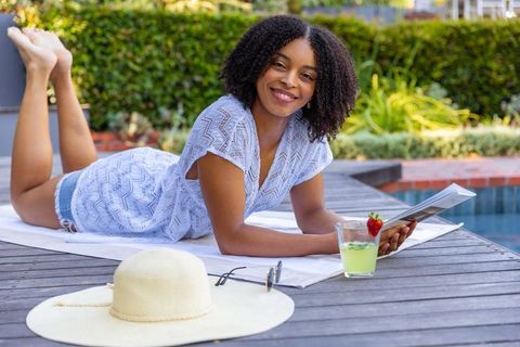 African american woman reading magazine poolside, smiling, enjoying refreshing summer drink