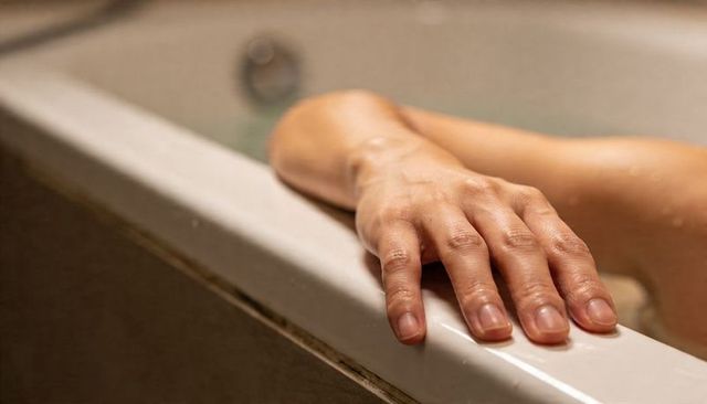 Relaxing hand resting on glossy bathtub rim with water droplets, minimalist bathroom calm