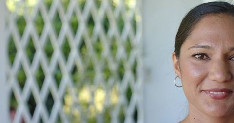 Smiling adult woman closeup in doorway wearing hoop earring with lattice and sunlight