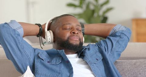Bearded man relaxing on sofa with wireless headphones enjoying music at home