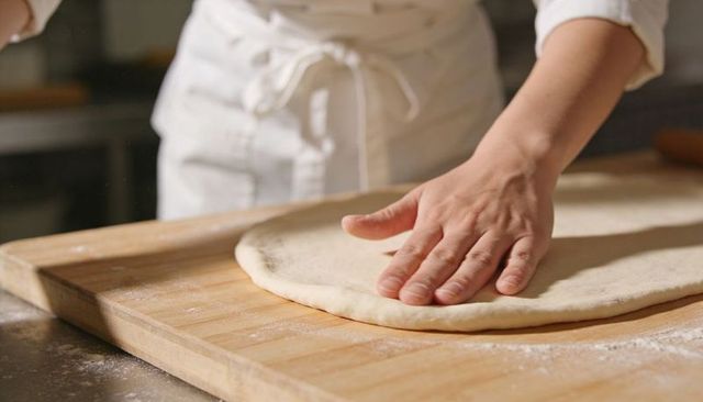 Shaping pizza dough by hand on wooden board in artisan bakery kitchen