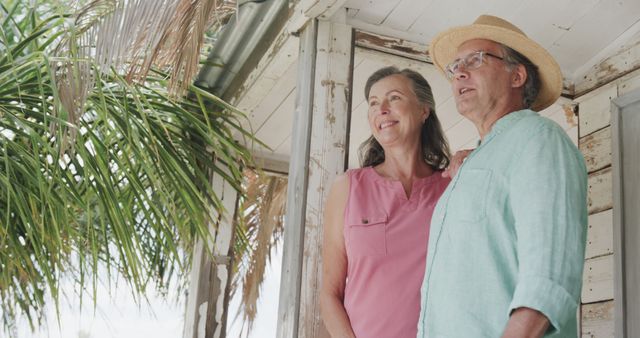 Happy senior caucasian couple embracing outside house on beach, copy space. Senior lifestyle, nature, relaxation, vacation, summer and leisure, unaltered.