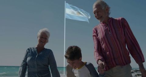 Elderly couple and grandchild ambling along beach with flag
