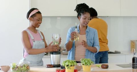 African women cooking together in bright modern kitchen, preparing smoothie and salad