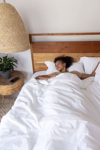 African american woman relaxing in bright minimalist bedroom under white duvet