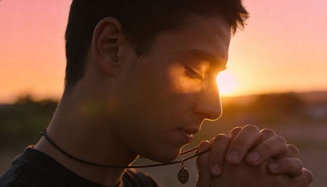 Teen male praying at sunset holding pendant necklace, quiet contemplation and devotion