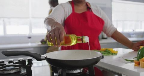 Woman Pouring Oil into Frying Pan in Modern Kitchen