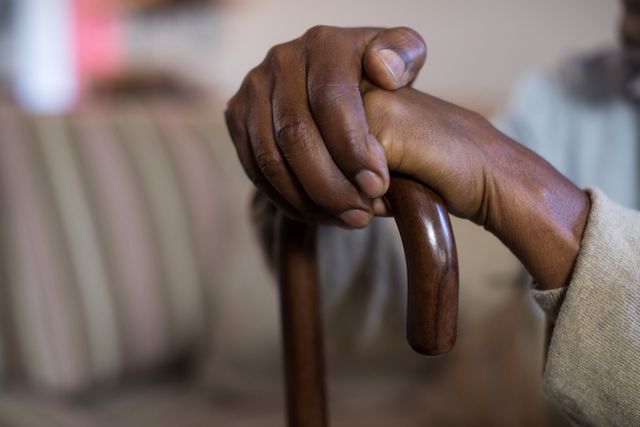 Close-up of senior man's hand holding a walking cane at home. Useful for topics related to elderly care, support, healthcare, retirement, and lifestyle of aged individuals. Ideal for articles, blogs, and advertisements focusing on senior living, mobility aids, and home care services.