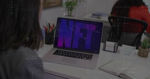 Two women working at modern coworking desk displaying nft on laptop, digital collaboration