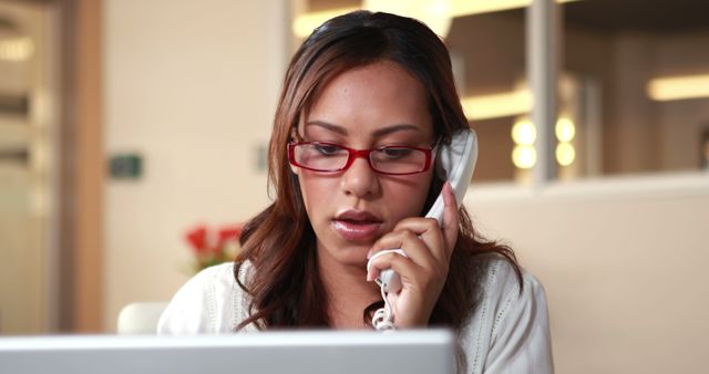 Woman using telephone while looking at computer screen in modern office environment. Perfect for business communication, customer service, corporate teamwork, and modern office technology concepts.