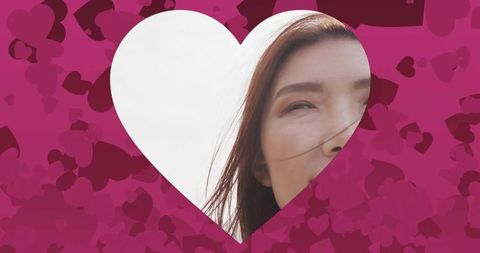 Chinese woman peeking through magenta heart frame with windblown hair
