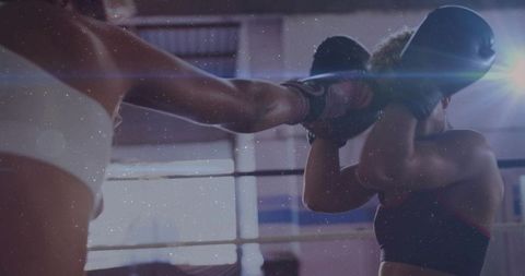 Female boxers sparring in ring with defensive guard, glove strike and dramatic backlight flare