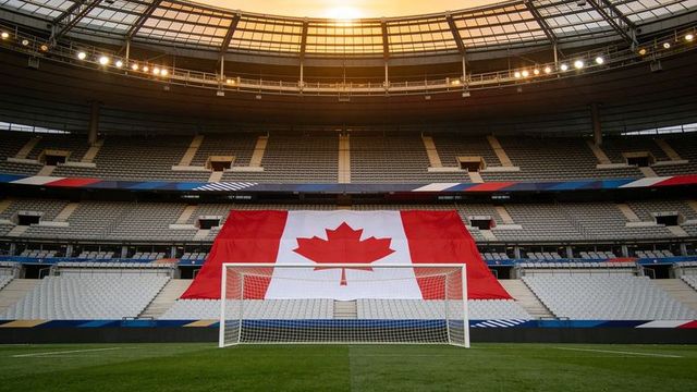 Canadian flag draping over empty stadium stands behind centered soccer goal at golden hour