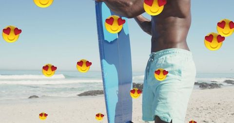 African american man with surfboard and emojis on beach