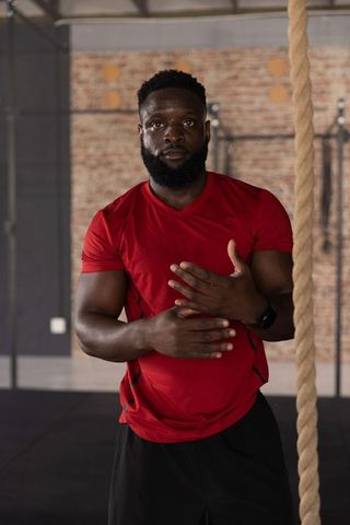 African american athlete standing in gym wearing red shirt preparing for rope climb