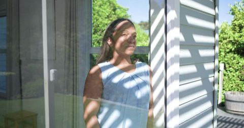 Mature woman basking in striped sunlight through sliding glass door