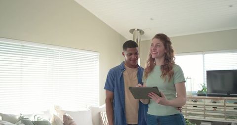 Young couple standing in bright modern living room holding tablet and planning home design
